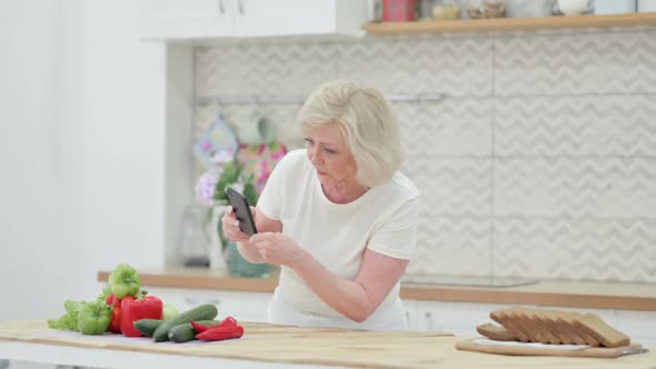 Old Woman Making Online Payment on Smartphone in Kitchen