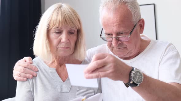 Elderly Husband and Wife Sit in White Living Room and Review Treatment Cards