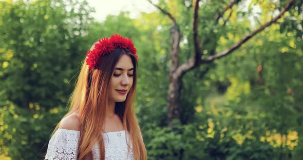 Beautiful Woman with a Rim on the Head Walks Near the Trees in the Park in Summer