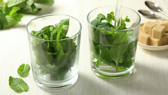  Pouring hot water in glasses with mint leaves to make mint tea