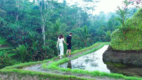 Young man and woman walking around a wet cliff whilst exploring a rice field farm in Indonesia