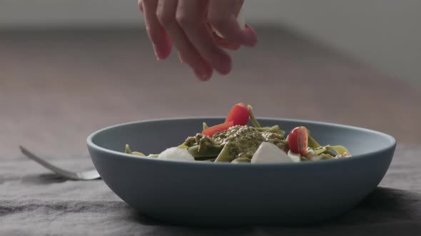 Slow Motion Man Hand Add Mozzarella Balls to Green Fettuccine with Pesto in Blue Bowl