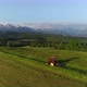Tractor mowing the grass with beautiful high mountains in the background, aerial view. - VideoHive Item for Sale