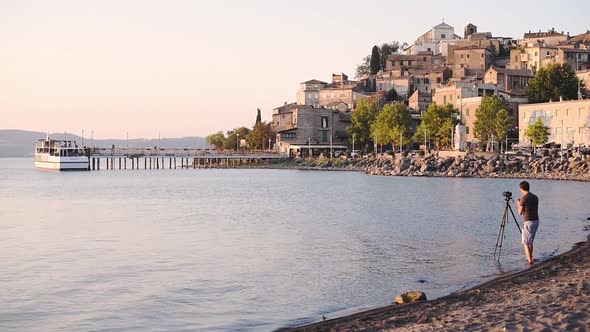 A Landscape Photographer Setting Up The Camera On A Tripod By The Shore Of Lake Trasimeno In Italy