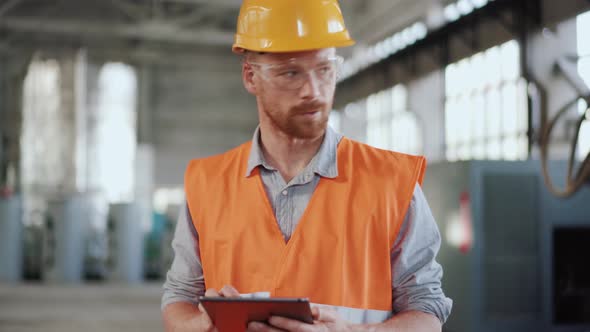 Serious man engineer in uniform calculating on tablet