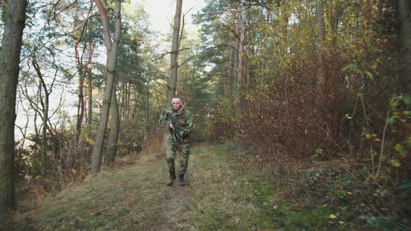 Soldier with Soot Strips on Face Jogging with Rifle in Forest and Looking Around
