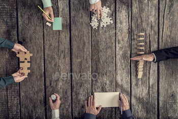 team of six businessmen holding puzzle pieces, writing down ideas on paper and stopping domino effect, top view.