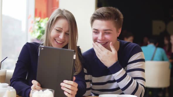Young Attractive Couple Using Digital Tablet Computer Looking at the Screen in Cafe