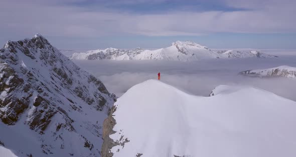 Aerial drone view of a mountain climber skier on the peak summit top of a snow covered mountain