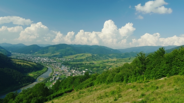 A Small Village Near the River. Against the Background of the Mountains Covered with Forest. Ski