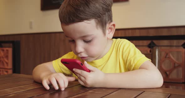 Portrait of a Child Looking at the Phone Sitting at the Table a Preschool Kid Uses Artificial