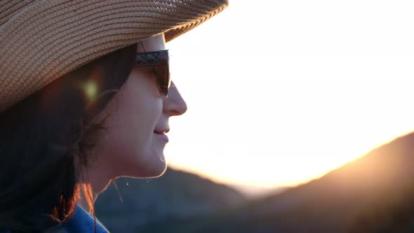 Closeup Smiling Beautiful Face of Travel Woman in Hat and Sunglasses at Mountain Sunset Background