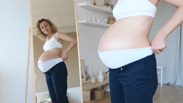 Clothes For Pregnant Women. Woman In Blue Trousers With High Waist Looking In Mirror