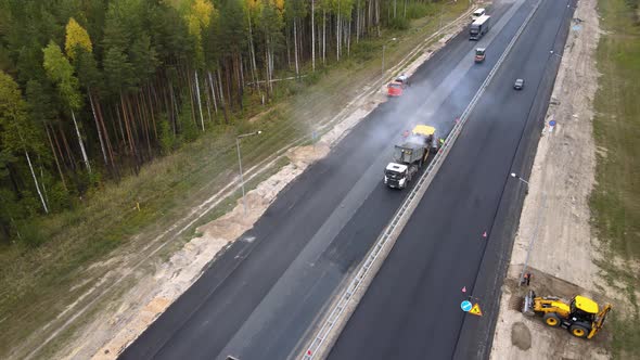 Workers in overalls are laying a new smooth road surface using heavy equipment