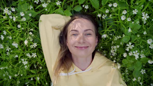 Beautiful Young Woman Lying on the Grass Against the Background of Flowers in the Forest