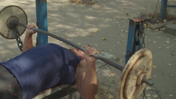 Athletic Man Doing Exercises with Barbell on Bench