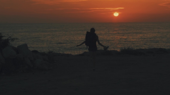 Young Girl Traveler with a Backpack and Straw Hat Running in Cyprus To the Sun and Sea at Sunset and