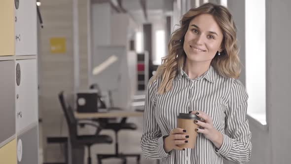 Happy Caucasian Businesswoman Posing for Photo Holding Coffee in Hand in Office