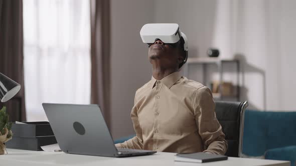 Using Virtual Reality for Education Young Black Guy is Wearing Headmounted Display Sitting at Table
