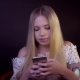 Young Blonde Is Smiling on a Black Background. It Prints a Text Message on the Smartphone - VideoHive Item for Sale