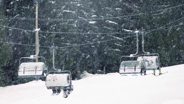 Skiers On Chairlift With Snow Falling