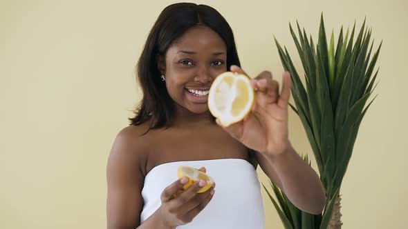 Afro American Woman Holding Lemon Halves in Hands Over Light Background in Spa Centre