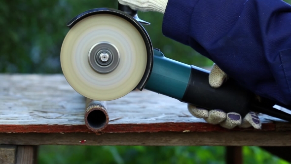 Worker in Gloves Cutting a Metal Pipe in Two Pieces