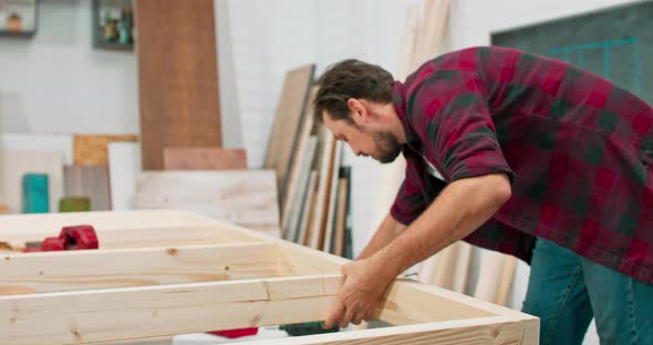 Concentrated Young Bearded Passionate Carpenter Drives a Carpentry Screw Into a Construction Beam