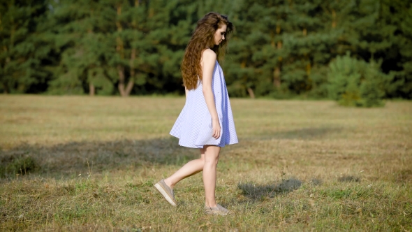 An Adult Girl with Long Curly Hair, Dressed in a Short Sarafan Walks the Field on a Warm Summer Day