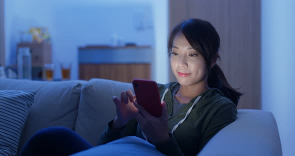 Asian woman use of cellphone sit on sofa at home in evening