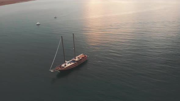 Aerial of two friends jumping from a wooden luxury sailboat during sunset