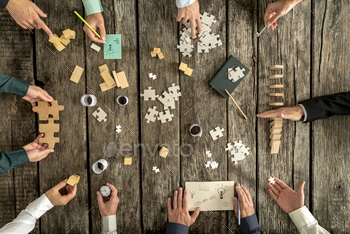  team of ten businessmen organizing strategy while holding puzzle pieces, writing down ideas on paper and rearranging wooden blocks, top view.