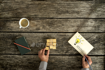  with an overhead view of a businessman sitting at a rustic table with building blocks and a hand drawn lightbulb on paper with text Vision.