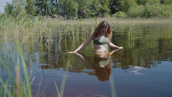 Young Woman Stands in River Water Watching Own Reflection