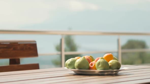 Green figs and apricots on a plate on a table outdoors