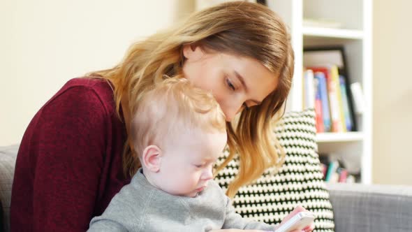 Mother and baby using mobile phone on sofa 4k