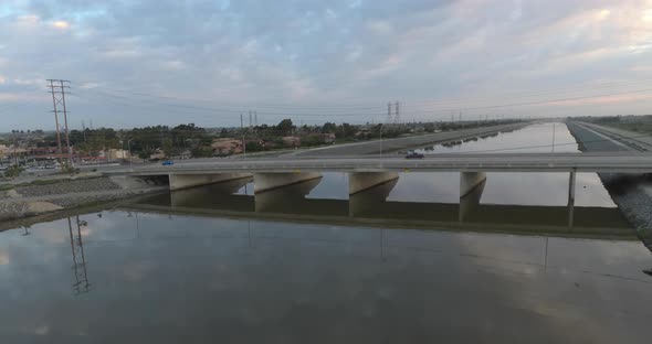 A drone flying above water advances towards cars driving over a bridge.