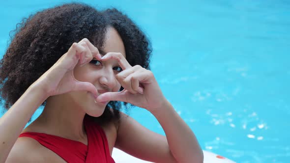 Curly American Teenager Girl Relaxing in Pool Smiles Folds Her Hands in Heart Sign in Front of Her