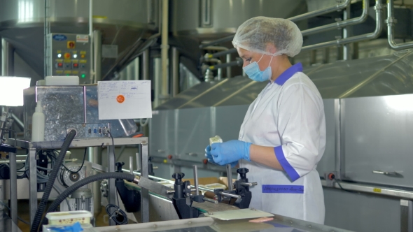 A Factory Operator in a Plastic Cap and a Mask Checks Cheese Packages