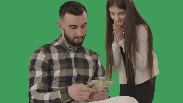 Handsome Caucasian Man Counting Money As Teenage Girl Rubbing Palms at the Background. Portrait of