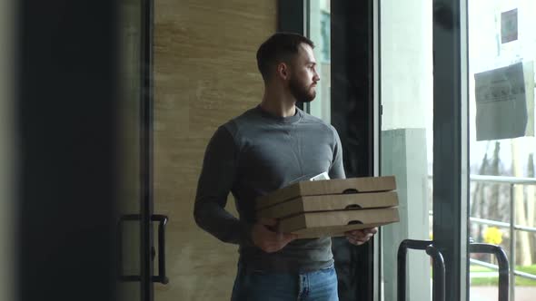Tracking Shot of Courier with Boxes Pizza Standing at Lobby Near Glass Door of Apartment Building
