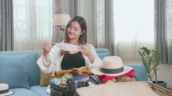 Asian Woman Packing Clothes And Protect Mask In A Suitcase For A New Journey. Luggage For Travel