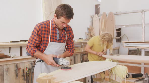 Two Caucasian male surfboard makers working in their studio and making a wooden surfboard together