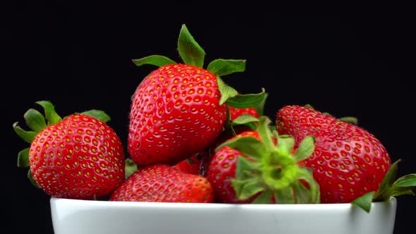 Appetizing strawberries with wilted green leaves lie on white porcelain bowl