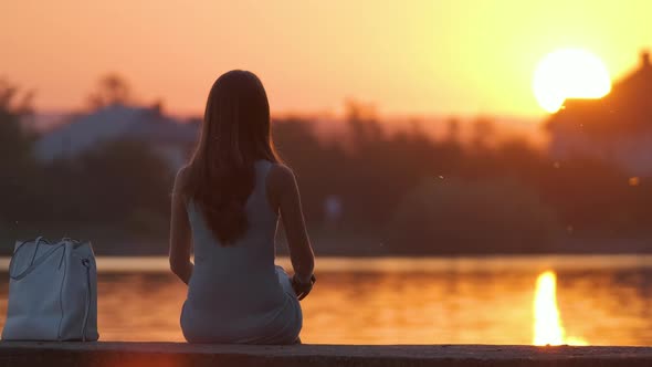 Lonely Woman Sitting Alone on Lake Shore on Warm Evening