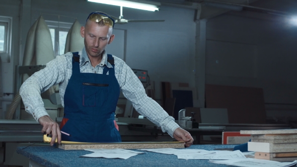 Worker Measuring Plank in Shop