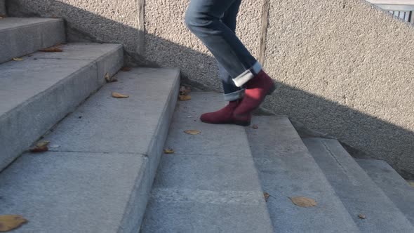 Female Legs in Burgundy Boots and Blue Jeans Climb the Stone Stairs