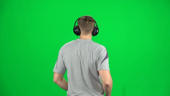 Man in Big Headphones Goes, Listening Music and Dancing on Green Screen at Studio. Back View. Slow