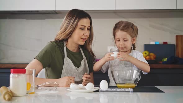 Mother Looks at Daughter in Apron Cracking Egg Into Bowl