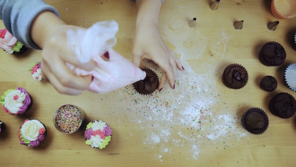 Top View of Young Female Hands Decorating the Chocolate Cupcake or Muffin with Cream, Using Pastry
